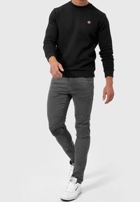 Zwarte sweatshirt met textuur en geribbelde manchetten, gecombineerd met grijze slim-fit jeans met kniestukken, en witte high-top sneakers.