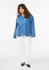 Blå denimskjorte med krave og lange ærmer, kombineret med hvide bukser med lige ben og sorte sko med spids tå.