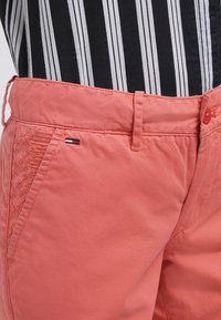 Szorty w kolorze koralowym z teksturowanym bocznym panelem. Charakteryzują się dopasowanym krojem, płaskim przodem i haftowanymi detalami, podkreślonymi małym logo.