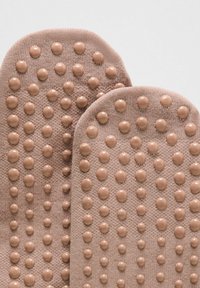 Artimiausiu planu du smėlio spalvos megzti padeliai su apvaliais, iškiliais guminiais taškais, išdėstytais spiralinėje schemoje, skirti sukibimui ar masažui.