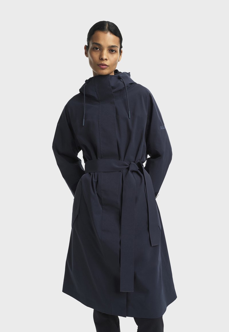 Cappotto con cappuccio blu navy realizzato in tessuto morbido, con vita cintrata e cintura da annodare, maniche lunghe e tasche laterali. Design minimalista.