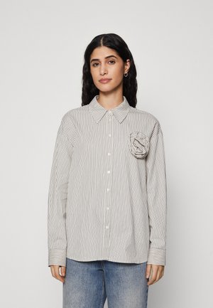 Button-up shirt in light cream with vertical black stripes, featuring a chest pocket with folded fabric detail and long sleeves.