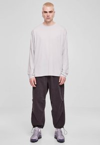 Camicia a maniche lunghe grigio chiaro con vestibilità rilassata, abbinata a pantaloni scuri e larghi e sneakers grigie. La camicia ha una scollatura rotonda.