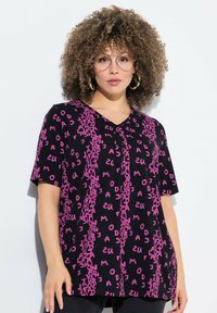 Camisa negra de manga corta con texto rosa en vertical y en negrita. Diseño de escote en V con un ajuste relajado y textura suave.