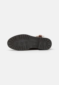 Bota de cuero marrón con una suela de goma texturizada. Presenta un patrón de banda de rodadura resistente, una marca mínima y un acento de hebilla lateral.