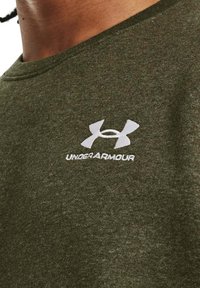 Olijfgroene katoenen t-shirt met korte mouwen en een ronde hals. Bevat een wit Under Armour-logo aan de bovenlinkerzijde.