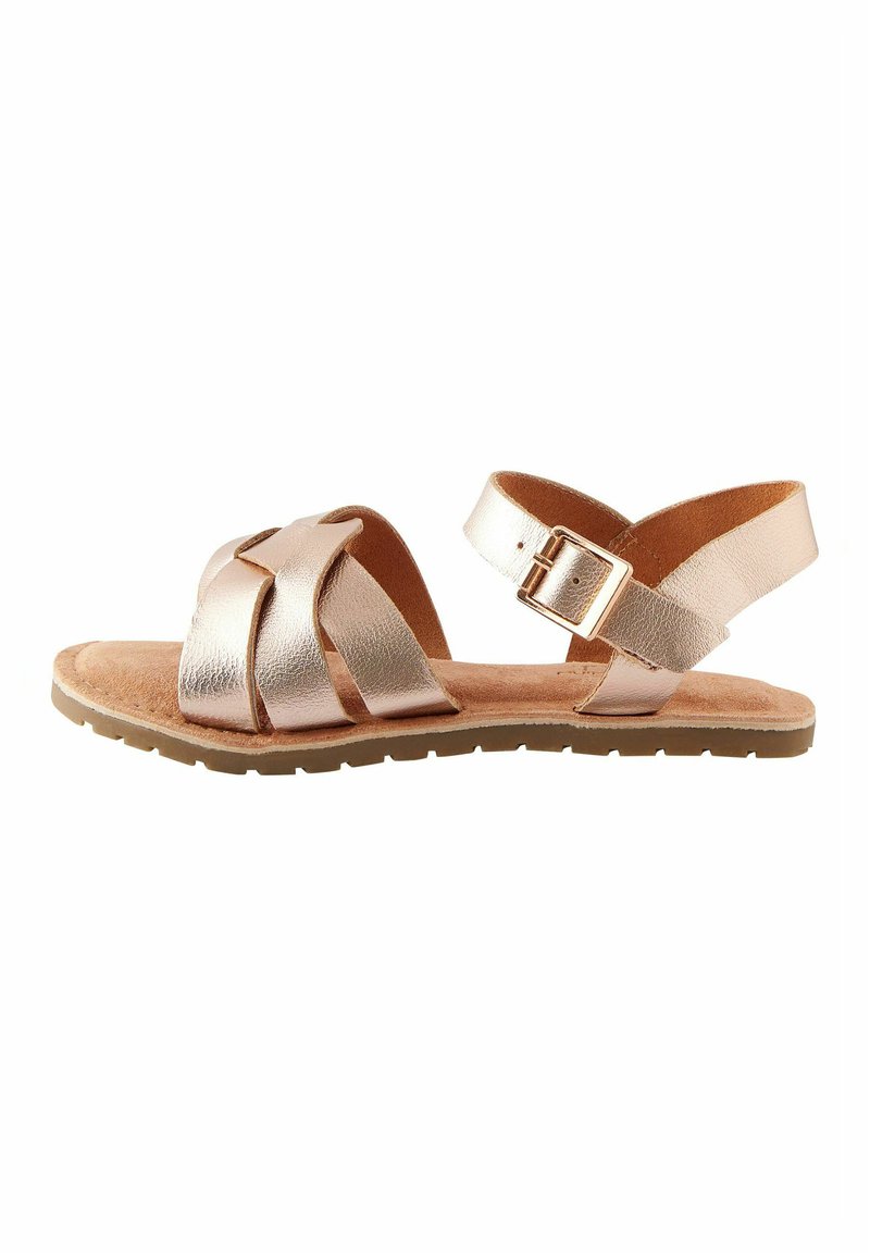 Sandali piatti in pelle metallizzata color oro rosa con strisce incrociate, cinturino alla caviglia con fibbia e suola beige testurizzata.