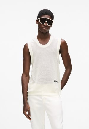 Fehér hálós atléta kerek nyakkivágással és bordázott szegéllyel, fehér nadrággal párosítva. Fekete márkajelzés a bal alsó oldalon.