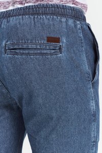 Pantaloni din denim albastru închis cu un tiv elastic, buzunar posterior cu deschidere orizontală și un mic patch de logo maro.