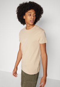 Beige katoenen crew neck t-shirt met korte mouwen, met een klassieke pasvorm en een gladde textuur. Draagt met olijfgroene cargo broek.