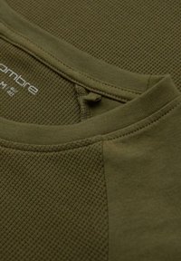 Vihreä oliivinvärinen teksturoitu kangast-paita, jossa on sileä kaulus ja kontrastivärinen kudottu kuvio vartalossa; kauluksessa on etiketti.