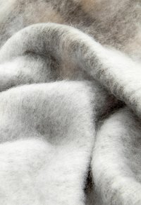 Un tissu en laine doux et gris avec une surface texturée et duveteuse. Des plis délicats créent une apparence en couches, avec des variations de gris clair et foncé.