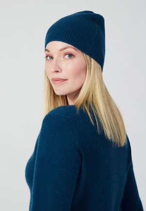 Teal geribde muts in combinatie met een getextureerde teal trui. De trui heeft een ronde hals en lange mouwen, wat een zachte, comfortabele uitstraling geeft.