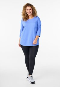 Lichtblauw, langarm shirt met een ronde hals, gecombineerd met zwarte leggings en grijze sportschoenen, met een relaxte pasvorm en een gladde textuur.