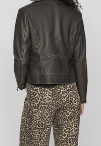 Schwarze Kunstlederjacke mit strukturierten Schultern und einem taillierten Schnitt, kombiniert mit beigen Hosen mit einem Leopardenmuster.
