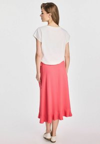 Biała bluzka z krótkim rękawem w połączeniu z zwiewną koralową spódnicą. Spódnica ma falbaniaste wykończenie, wykonana jest z gładkiego materiału. Uzupełniona jasnymi butami.