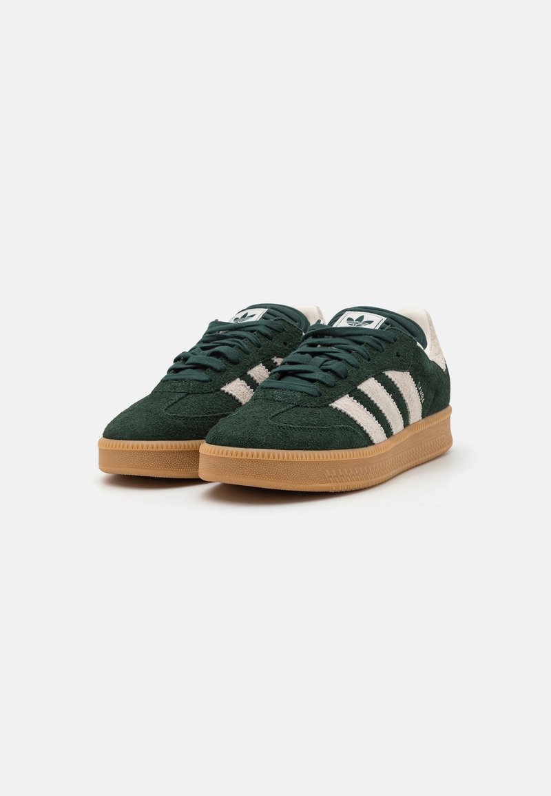 Baskets en suede vert avec des rayures blanches, design à lacets rond, et semelle en caoutchouc beige. Tige texturée et détail de marque classique.