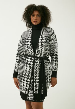 Cardigan à motifs noir et blanc avec manches longues, design enveloppant et ceinture nouée. Présente des formes géométriques et abstraites tout au long.