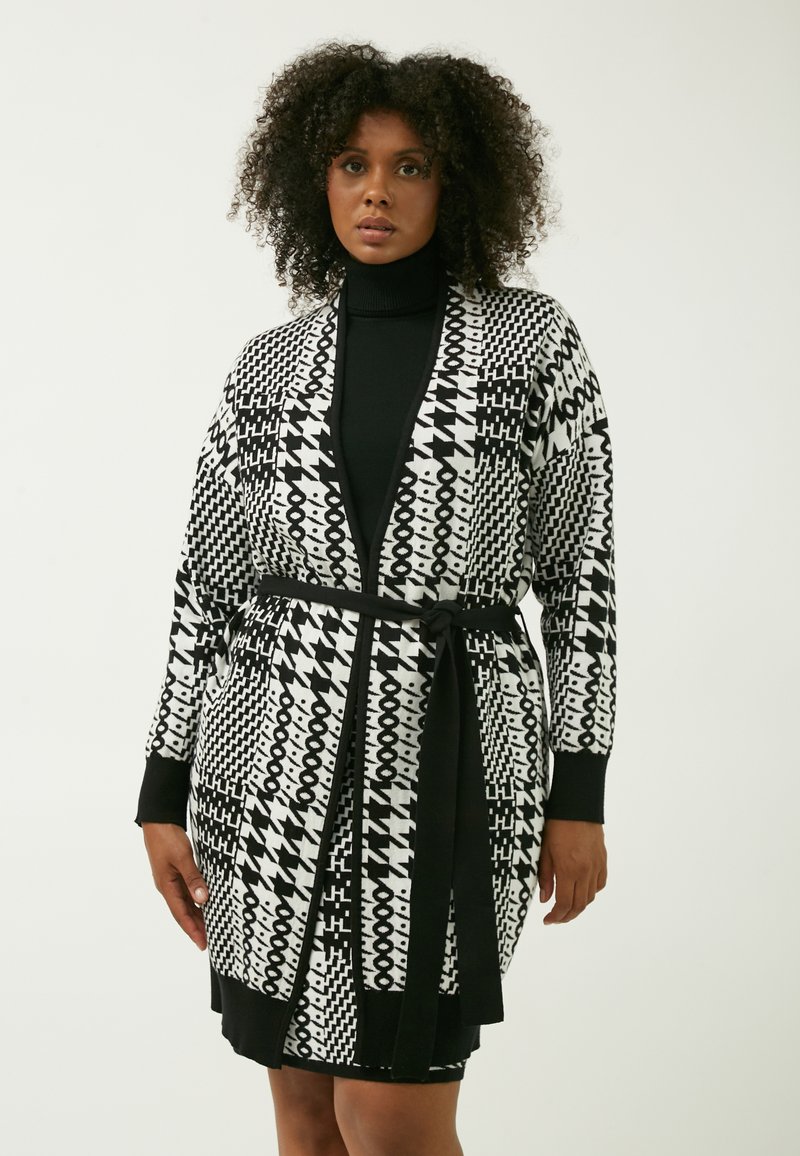 Cardigan bianco e nero con motivo a strisce, maniche lunghe, design a incrocio e cintura legata. Presenta forme geometriche e astratte su tutta la superficie.