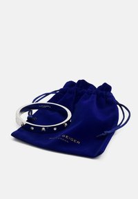 Bracciale in argento con strass trasparenti, appoggiato su un sacchetto di velluto blu navy con testo dorato.