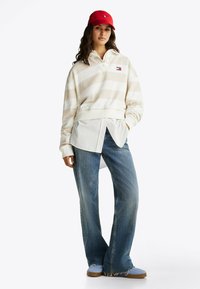 Romige gestreepte pullover met een kraag, gecombineerd met een witte overhemd, blauwe wijde jeans en een rode pet, met casual schoenen.
