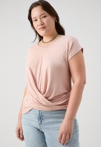 Ανοιχτό ροζ μπλούζα κοντό μανίκι με σχέδιο στριμ�μένου μπροστινού μέρους, κατασκευασμένη από λείο ύφασμα. Συνδυάζεται με ανοιχτό μπλε τζιν παντελόνι.