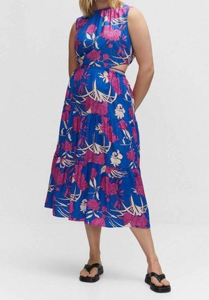 Femme portant une robe midi bleue sans manches à imprimé floral rose avec des découpes latérales, associée à des sandales compensées noires.