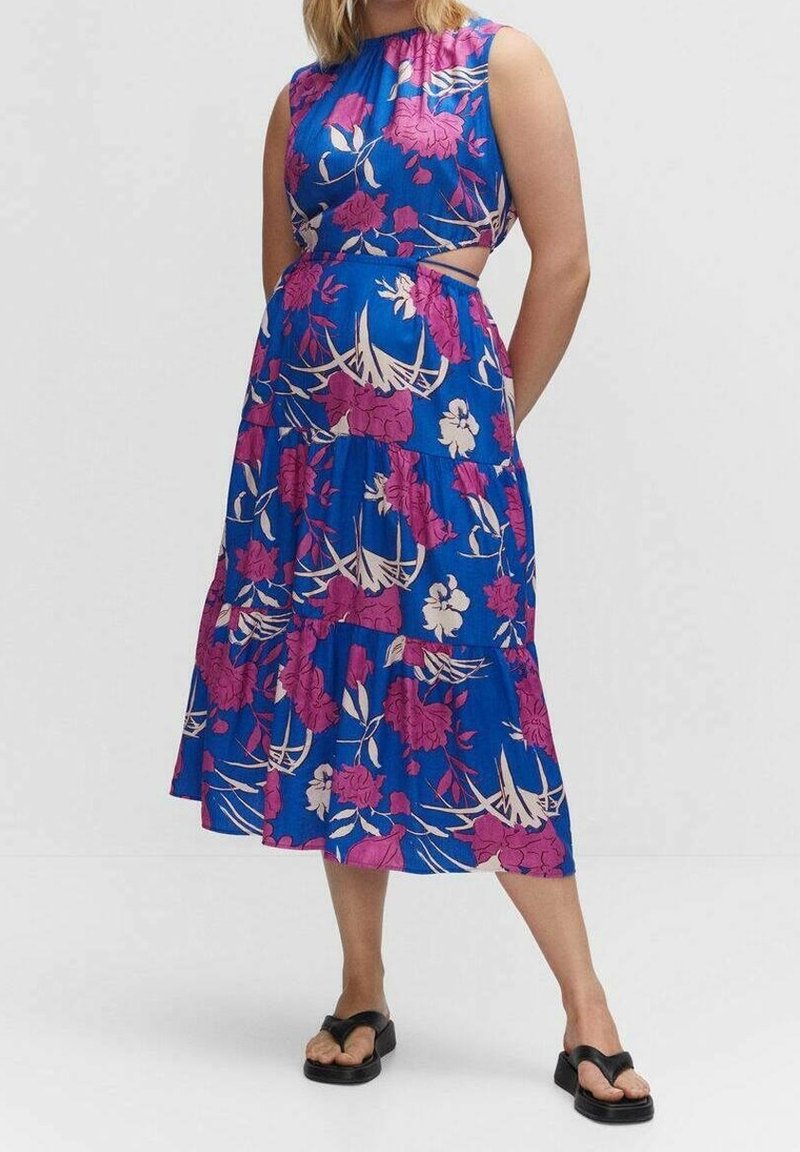 Femme portant une robe midi bleue sans manches à imprimé floral rose avec des découpes latérales, associée à des sandales compensées noires.