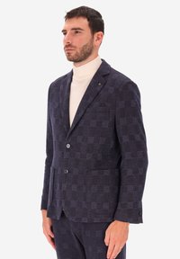 Blazer a scacchi blu con una consistenza morbida, due bottoni, revers a punta e tasche a patta, abbinato a un dolcevita crema.