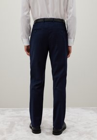 Pantalones de vestir a cuadros en tono marino, confeccionados con una tela tejida, que presentan un corte ajustado, presillas para cinturón y dos bolsillos traseros. Zapatos negros de acabado liso.