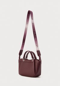 Sac à main en cuir bordeaux avec finition texturée, poignées supérieures doubles et bandoulière ajustable dégradée avec logo de la marque en relief.