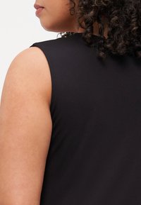 Top negro sin mangas con una textura suave, que presenta un escote redondo y un diseño ajustado, destacando un primer plano del hombro y el brazo.