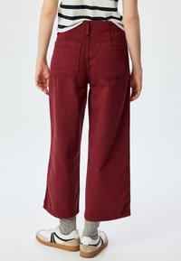 Bordeaux wijde broek van katoen, met een hoge taille, twee achterzakken en een relaxte pasvorm. Gemaakt met witte sneakers en grijze sokken.