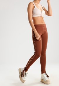 Leggings marrones con detalles de encaje en los laterales, combinados con un top corto de canalé ligero. El calzado presenta suelas gruesas con un diseño sencillo.