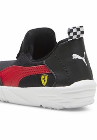 Fekete és piros sportcipő sima szövet felsőrésszel, fehér gumitalppal és kockás húzófüllel. Jellemzője egy sárga Ferrari logó akcentus.