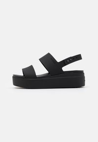 Black platform sandals featuring wide straps and an adjustable ankle strap. Made of synthetic material with a textured footbed and solid sole.