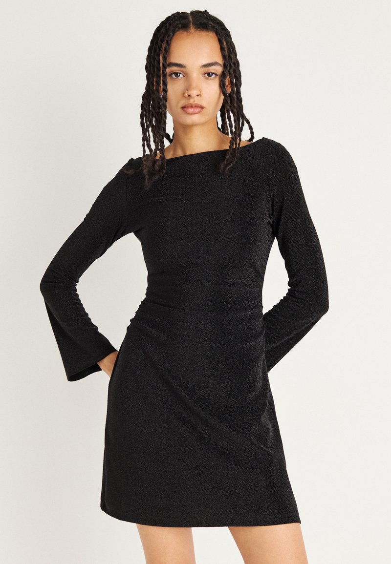 Abito lungo nero a maniche lunghe con silhouette aderente, scollatura a barca e polsini svasati. Realizzato in un tessuto testurizzato e luccicante.