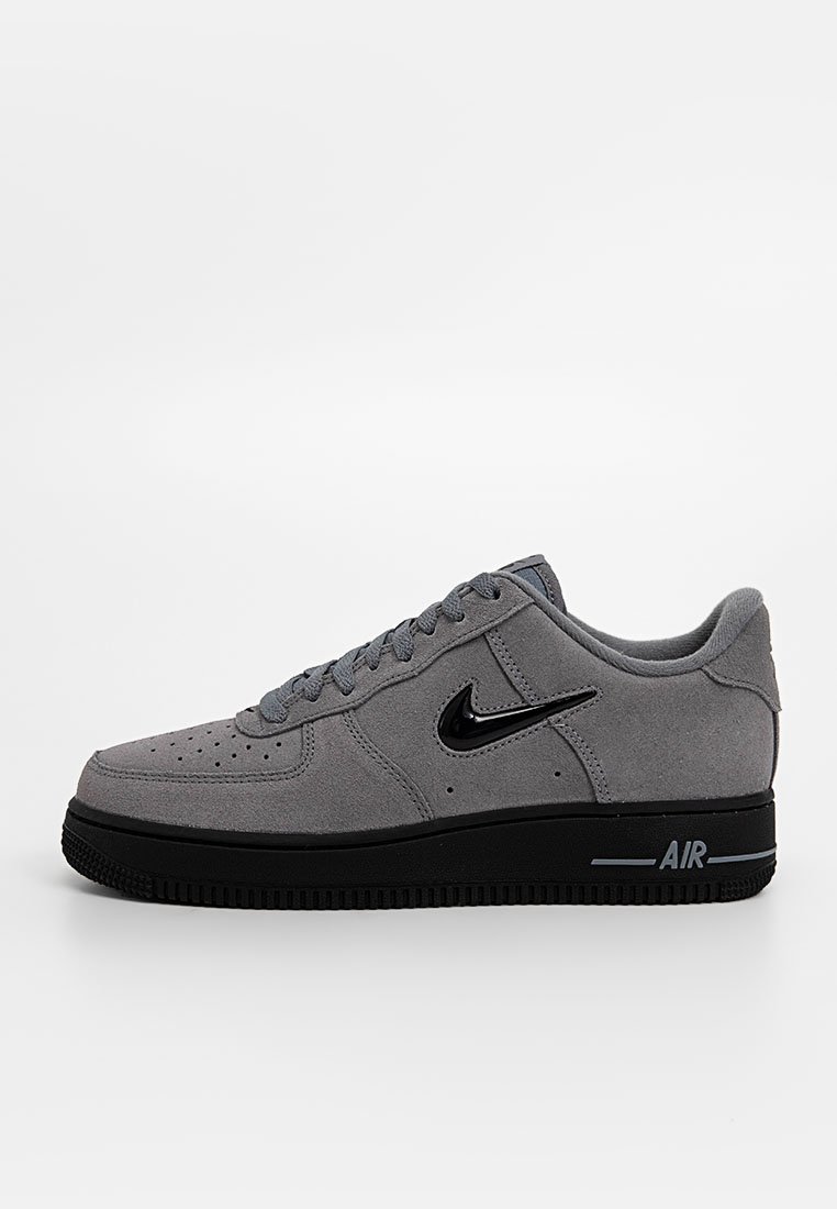 Zapatilla de aire Nike de ante gris de corte bajo con suela negra, logo de swoosh negro y cordones grises, mostrada en perfil lateral sobre fondo blanco.