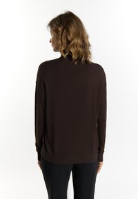 Brauner Strickpullover mit langen Ärmeln, einem hohen Kragen und geripptem Saum. Weiche Textur und lockere Passform, von hinten gezeigt.