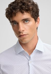 Patroon witte overhemd met een button-down kraag, met kleine blauwe geometrische ontwerpen en een gladde stoftextuur.