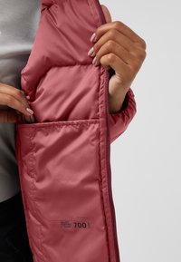Intérieur isolé de veste doudoune rose avec un tissu lisse, présentant une grande poche et un détail d'étiquette "Allied Feather + Down 700".
