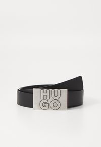 Črn usnjen pas z pravokotno, embosirano srebrno sponko, na kateri je v krepkih črkah napis "HUGO". Gladka tekstura in minimalističen dizajn.