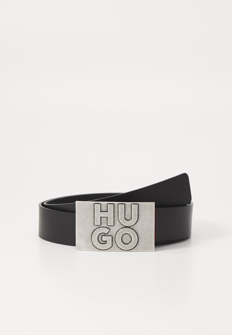 Črn usnjen pas z pravokotno, embosirano srebrno sponko, na kateri je v krepkih črkah napis "HUGO". Gladka tekstura in minimalističen dizajn.