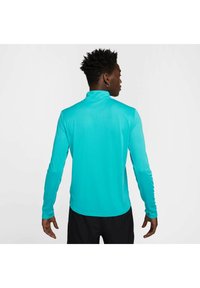 Lichtgewicht, langes sportshirt in helder turquoise, met een hoge kraag en een gladde textuur, gedragen met zwarte shorts.