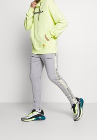 Neongul hoodie med svart logotyp, grå joggingsbyxor med sidobr märkning och moderna mångfärgade sneakers med luftdämpning.