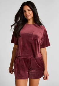 Velvet loungewear set in pruimkleur, bestaande uit een cropped top met korte mouwen en een zak, gecombineerd met bijpassende shorts met elastische tailleband. Zachte textuur overal.