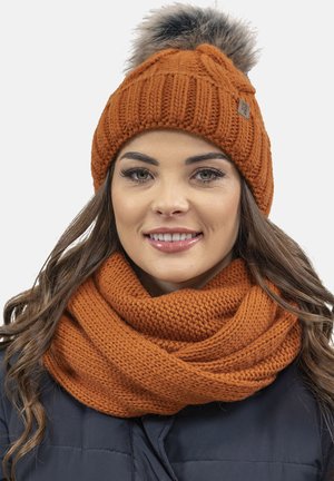 Knit orange beanie with a fluffy pom-pom and matching infinity scarf, featuring a textured pattern and chunky yarn.
