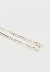 Ασημένιο κολιέ με αλυσίδα και κούμπωμα με σχήμα αστακού σε λευκό φόντο, που δείχνει κοντινό πλάνο των συνδεδεμένων μεταλλικών βρόχων.