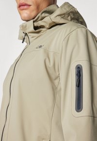 Beige jacket with a hood, featuring a zippered pocket on the left arm and a smooth, water-resistant texture. Subtle branding visible.