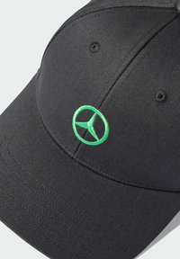 Svart basebollkeps av textured tyg, med en grön broderad logotyp på framsidan och en böjd skärm.